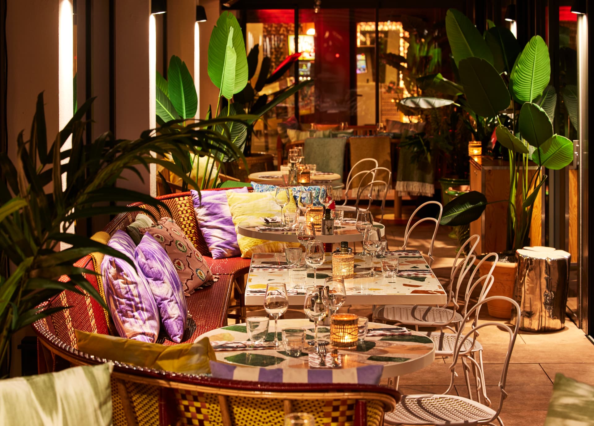 Terrasse du Mama Shelter à Dijon, banquettes de rotin, grandes plantes et tables éclairées à la bougie